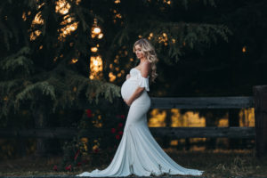 Maternity Photographer, Pregnant woman in a flowy white dress before a dramatic dark green foilage.