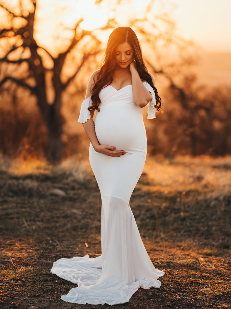 Maternity Photography, Pregnant woman in white dress with hand on her belly at golden hour
