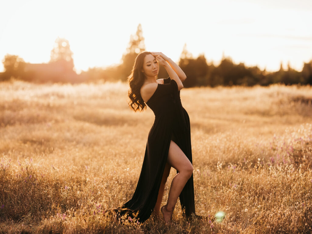 Maternity Photographer, a pregnant woman stands in a dry grassy field at golden hour wearing an elegant dress